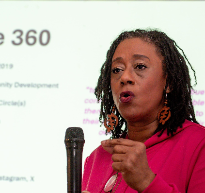 photo of a black woman middle-aged with a microphone speaking at an event